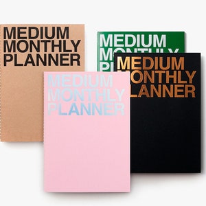 May include: A collection of medium monthly planners in various colors, including kraft, green, pink, and black. Each planner features the text "MEDIUM MONTHLY PLANNER" in bold, contrasting colors. The planners are arranged on a white background.