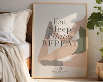 May include: A framed poster with the words "Eat Sleep Pilates Repeat" in a stylish font. The artwork features a person in a pilates pose, wearing a green leotard. The poster is part of the "Mind & Body Collection."