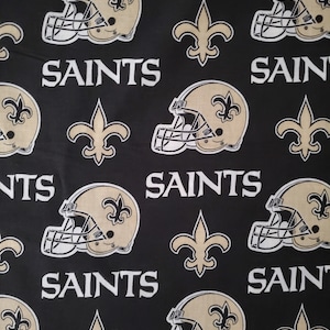 May include: Black fabric with a repeating pattern of gold football helmets, fleur-de-lis, and the word "Saints".