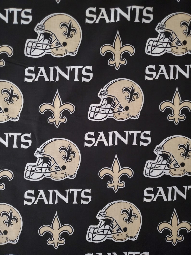 May include: Black fabric with a repeating pattern of gold football helmets, fleur-de-lis, and the word "Saints".