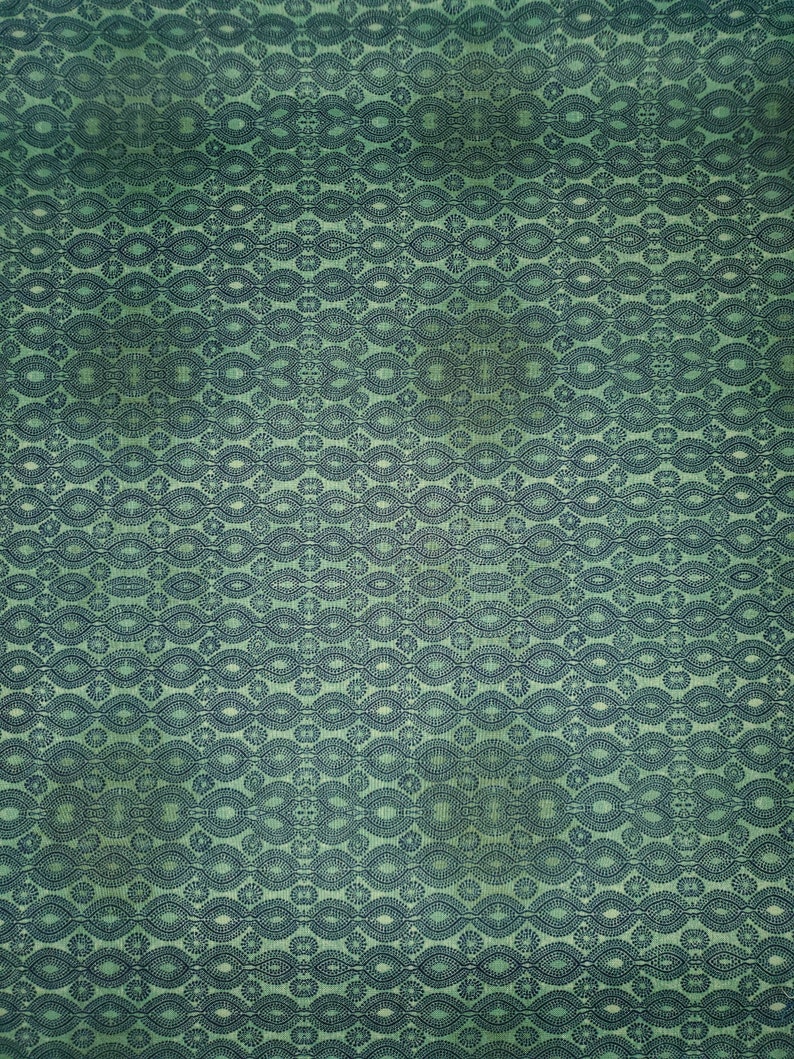 May include: A green fabric with a repeating pattern of dark blue ovals and circles.