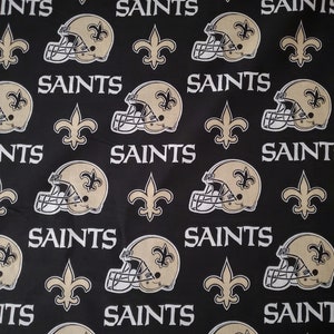 May include: Black fabric with a repeating pattern of gold football helmets, fleur-de-lis, and the word "Saints".