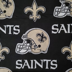 May include: Black fabric with a repeating pattern of white "Saints" text, gold fleur-de-lis, and gold football helmets with fleur-de-lis on the side.