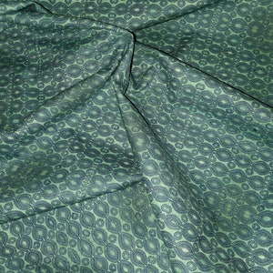 May include: Green fabric with a repeating pattern of dark blue ovals and circles. The fabric is folded and wrinkled.