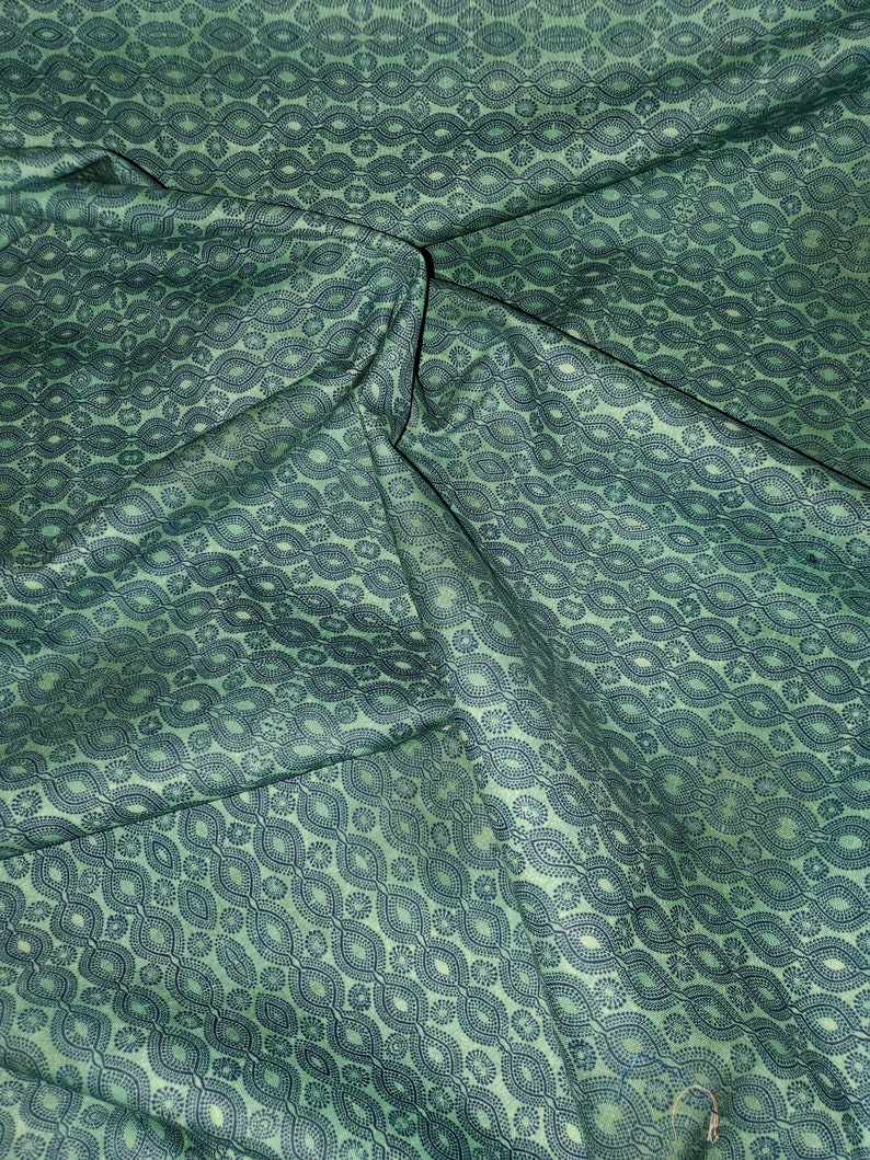 May include: Green fabric with a repeating pattern of dark blue ovals and circles. The fabric is folded and wrinkled.