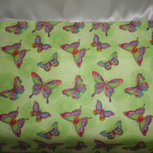 Puede incluir: Tela verde con un patr&oacute;n repetido de mariposas coloridas. Las mariposas tienen alas moradas, rosas, rojas, amarillas y verdes.