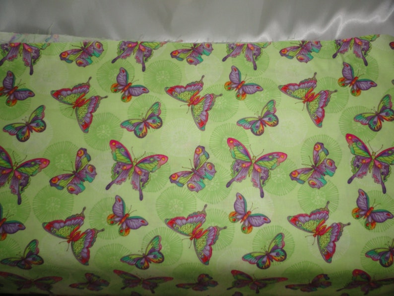 Puede incluir: Tela verde con un patr&oacute;n repetido de mariposas coloridas. Las mariposas tienen alas moradas, rosas, rojas, amarillas y verdes.