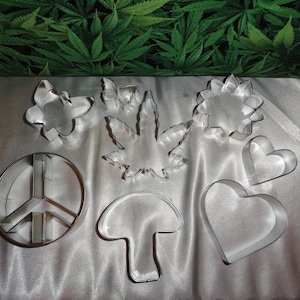May include: A set of nine metal cookie cutters in various shapes, including a peace sign, a mushroom, a heart, a flower, and a leaf. The cutters are silver and have a shiny finish.