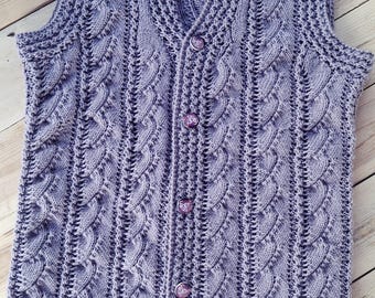 May include: A lavender-colored, sleeveless knitted vest with a V-neck and button closure. The vest features a textured cable knit design and decorative buttons. The garment is displayed on a wooden surface.