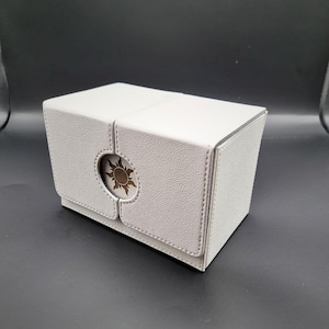 May include: A white leather card box with a sun design on the front. The box is closed and has a hinged lid.