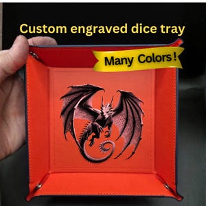 May include: Custom engraved dice tray with a dragon design. The tray is red with a blue border and features a detailed illustration of a dragon with outstretched wings. The text "Many Colors!" is displayed on a yellow banner.