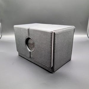 May include: A black leather card box with a stitched design and a circular cutout on the front.
