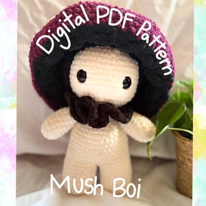 Puede incluir: Una figura de hongo de ganchillo con cuerpo color crema, ojos negros y una bufanda marrón oscuro. El sombrero del hongo es negro y burdeos. El texto "Digital PDF Pattern" y "Mush Boi" está escrito en la imagen.
