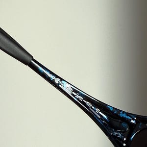 May include: Close-up of a black and blue patterned sunglasses arm. The arm has a glossy finish with blue accents and the word "Police" printed on the side. The sunglasses arm is set against a light background.