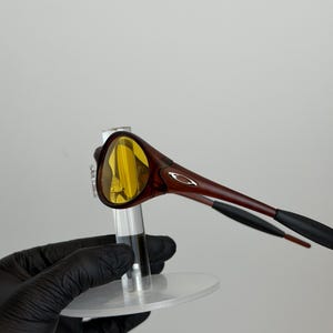 K&ouml;nnte beinhalten: Braune und gelb get&ouml;nte Sonnenbrille mit einem schlanken, modernen Design. Die Fassung ist in einem satten Braunton gehalten, mit einem dezenten silbernen Logo an den B&uuml;geln. Die Gl&auml;ser sind leuchtend gelb.