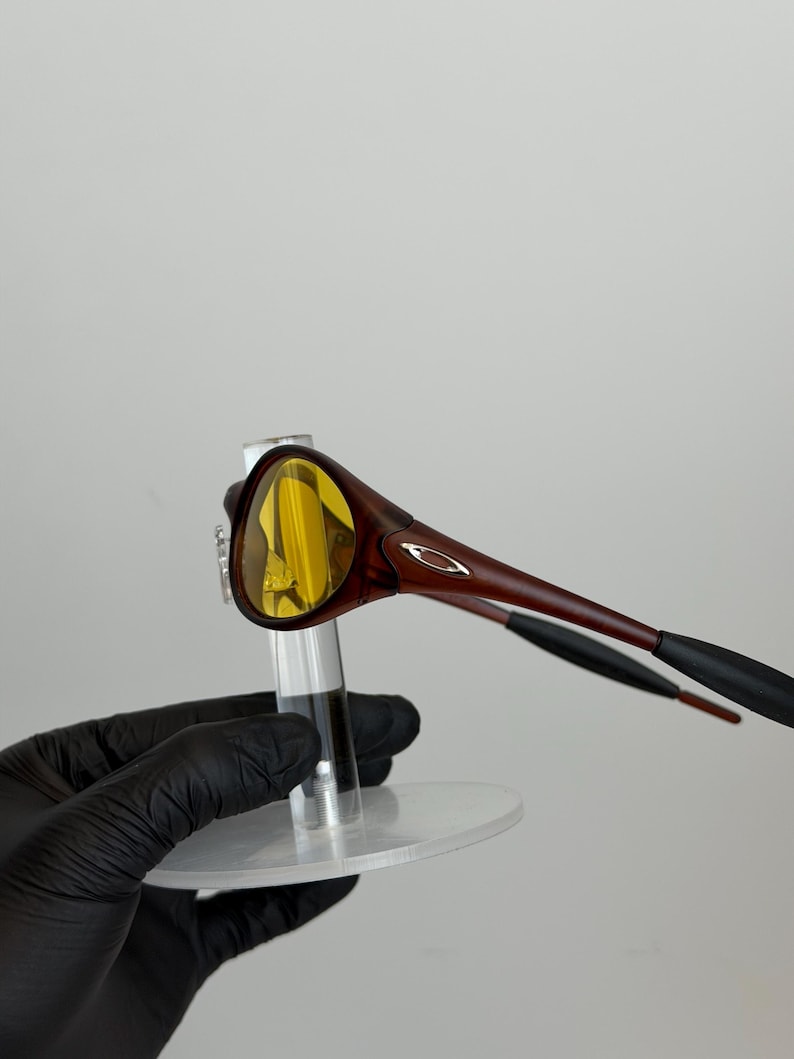 K&ouml;nnte beinhalten: Braune und gelb get&ouml;nte Sonnenbrille mit einem schlanken, modernen Design. Die Fassung ist in einem satten Braunton gehalten, mit einem dezenten silbernen Logo an den B&uuml;geln. Die Gl&auml;ser sind leuchtend gelb.
