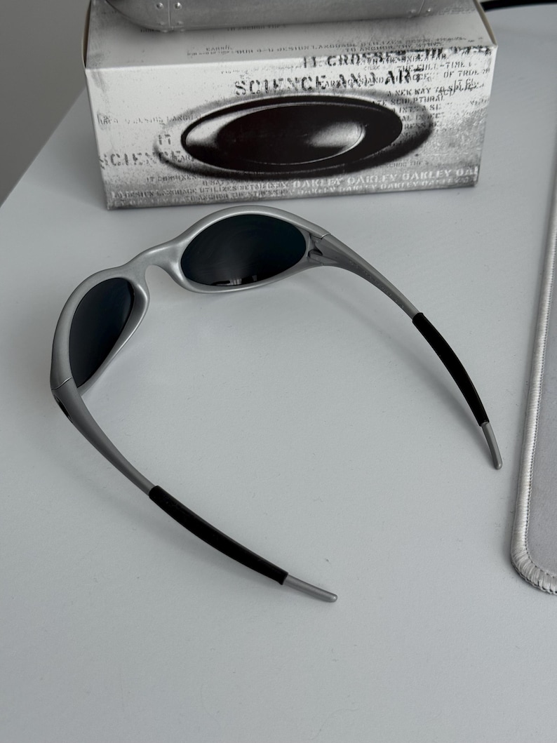 Pu&ograve; includere: Occhiali da sole con montatura argentata e lenti scure, dal design elegante e moderno. Le aste hanno impugnature in gomma nera per il comfort. Gli occhiali da sole sono esposti con la loro scatola originale, con la scritta "SCIENCE AND ART".