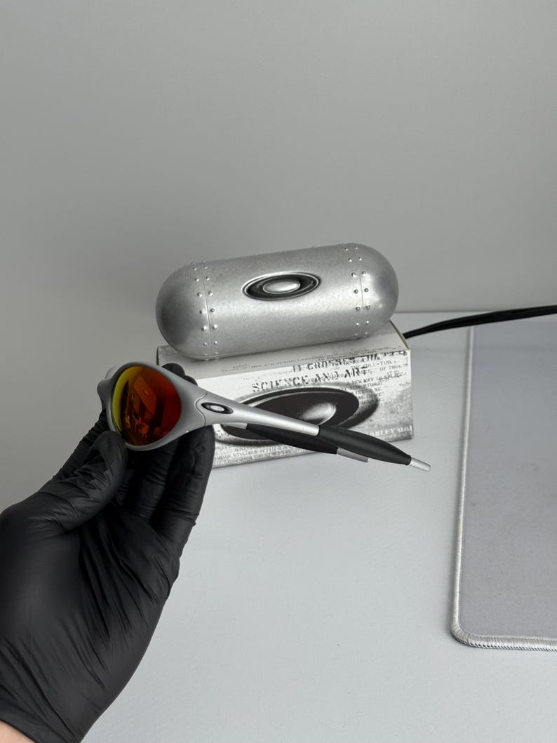 Pu&ograve; includere: Occhiali da sole argento e neri con lenti rosse. Gli occhiali da sole sono su una scatola con la scritta "SCIENCE AND ART". &Egrave; presente anche un astuccio argentato. Design elegante e moderno.