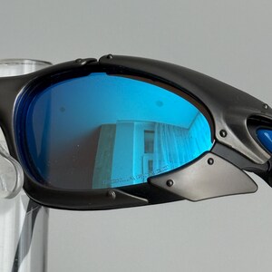 May include: Black sunglasses with blue polarized lenses. The lenses reflect the surrounding environment. The frame is black and has a sporty design. The word "POLARIZED" is printed on the lens.