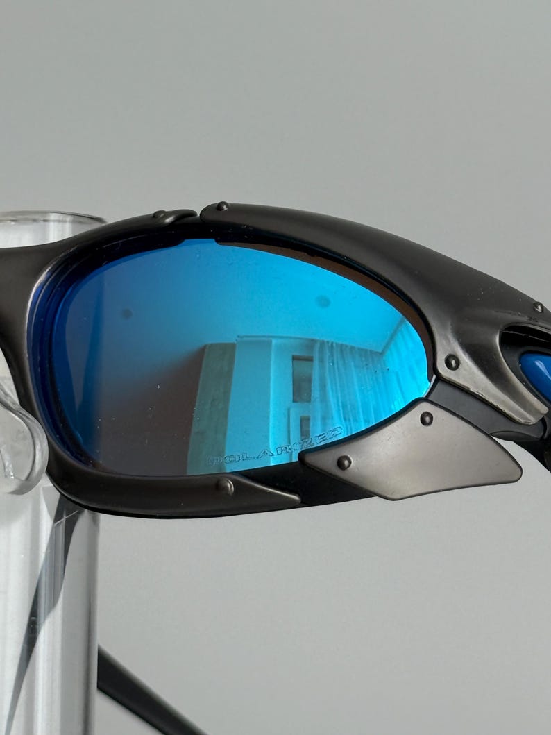 May include: Black sunglasses with blue polarized lenses. The lenses reflect the surrounding environment. The frame is black and has a sporty design. The word "POLARIZED" is printed on the lens.