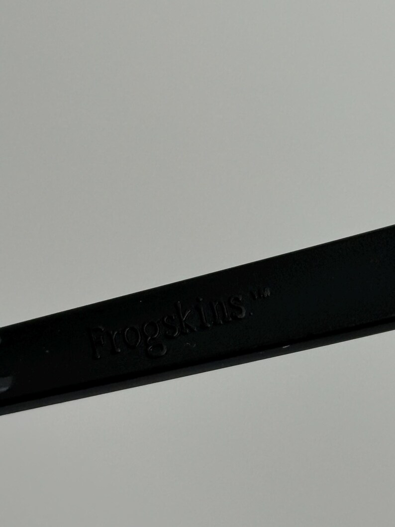 May include: A close-up of a black object with the word "Frogskins" embossed on it. The object is set against a plain, light gray background. The text is in a sans-serif font.