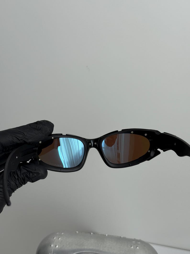 May include: Black sunglasses with a curved frame and tinted lenses. The lenses reflect blue and orange hues. The sunglasses have a sporty design.