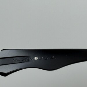 May include: Close-up of a black object with the text "MADE IN U.S.A." printed on it. The object has a curved shape and appears to be made of a solid material. The background is a plain, light gray.