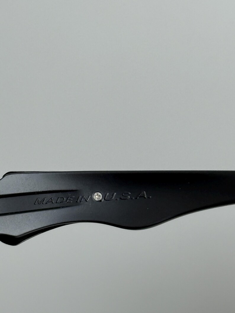 May include: Close-up of a black object with the text "MADE IN U.S.A." printed on it. The object has a curved shape and appears to be made of a solid material. The background is a plain, light gray.