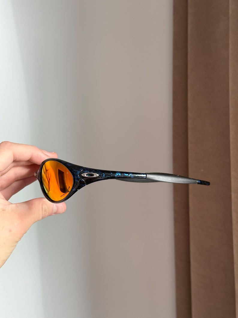 Puede incluir: Gafas de sol deportivas con montura negra y azul estampada y lentes naranjas. Las gafas de sol tienen un dise&ntilde;o elegante, perfecto para actividades al aire libre. Las lentes son reflectantes y la montura es ligera.