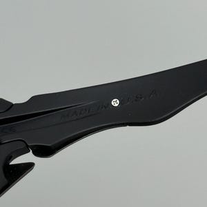 May include: Close-up of a black object with the text "MADE IN U.S.A." printed on it. The object has a sleek, modern design with sharp angles and a matte finish. The background is a solid, neutral gray.