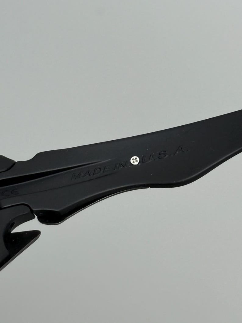 May include: Close-up of a black object with the text "MADE IN U.S.A." printed on it. The object has a sleek, modern design with sharp angles and a matte finish. The background is a solid, neutral gray.