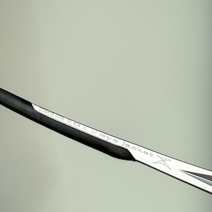 May include: Close-up of a silver and black eyeglass frame. The frame has the text "eye jacket" and other numbers and letters printed on it. The frame is angled diagonally across the image.