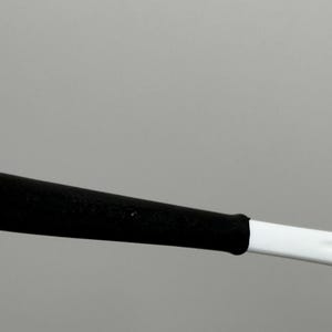 May include: A white and black object, possibly a sports equipment handle or a tool. The handle is white with a black grip. The image is set against a plain gray background.