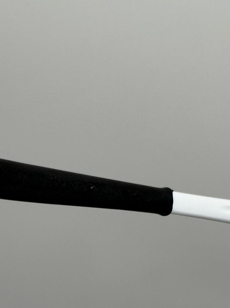 May include: A white and black object, possibly a sports equipment handle or a tool. The handle is white with a black grip. The image is set against a plain gray background.