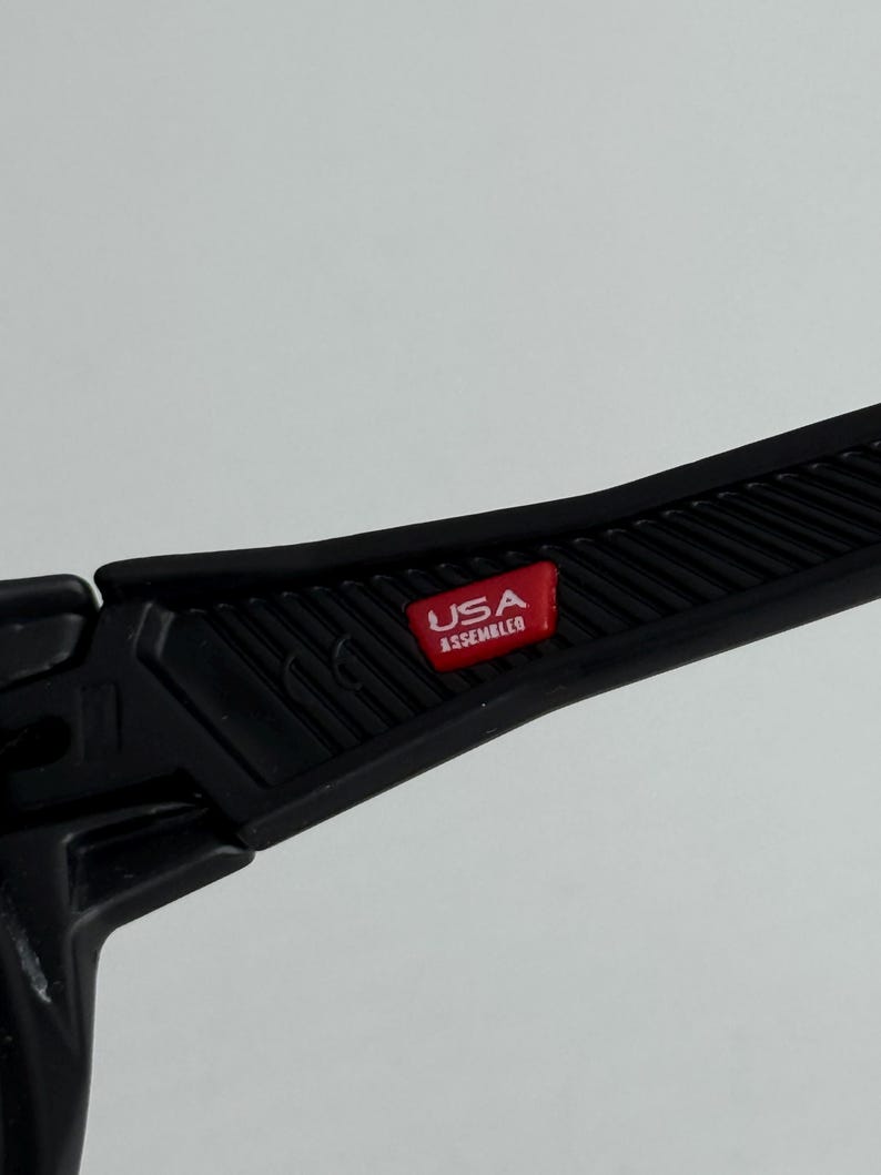 K&ouml;nnte beinhalten: Nahaufnahme eines schwarzen Kunststoffbauteils mit einem roten rechteckigen Emblem. Das Emblem zeigt "USA ASSEMBLED" in wei&szlig;er Schrift. Das Objekt hat eine strukturierte Oberfl&auml;che und ist Teil eines gr&ouml;&szlig;eren Produkts.