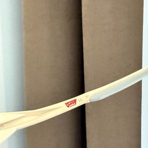 May include: A close-up of a light-colored, curved object with a red and white logo. The object is positioned in front of two brown cylindrical shapes and a white wall. The logo is partially visible.