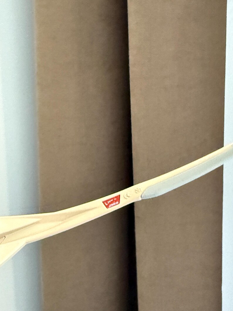 May include: A close-up of a light-colored, curved object with a red and white logo. The object is positioned in front of two brown cylindrical shapes and a white wall. The logo is partially visible.