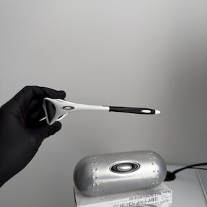 May include: White and black sports sunglasses with a silver case and a box. The sunglasses have a unique design with a white frame and black accents. The case is metallic silver with a matching logo.