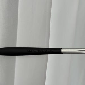May include: A black makeup brush handle with the text "MADEINU.S.A." printed in white. The handle transitions to a silver-colored metal brush head. The background is a white curtain.