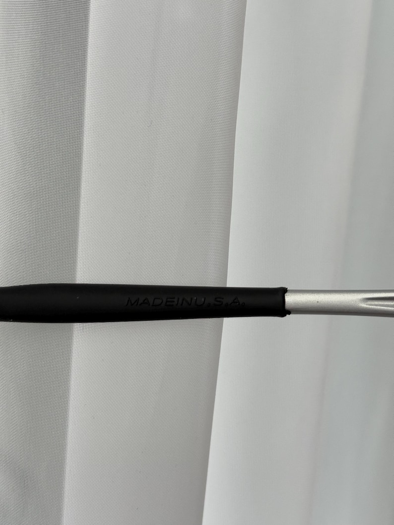 May include: A black makeup brush handle with the text "MADEINU.S.A." printed in white. The handle transitions to a silver-colored metal brush head. The background is a white curtain.
