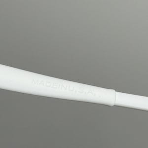 May include: Close-up of a white object with the text "MADE IN U.S.A." printed on it. The object appears to be a part of a larger item, possibly a handle or a component of a tool or device. The background is a solid grey.