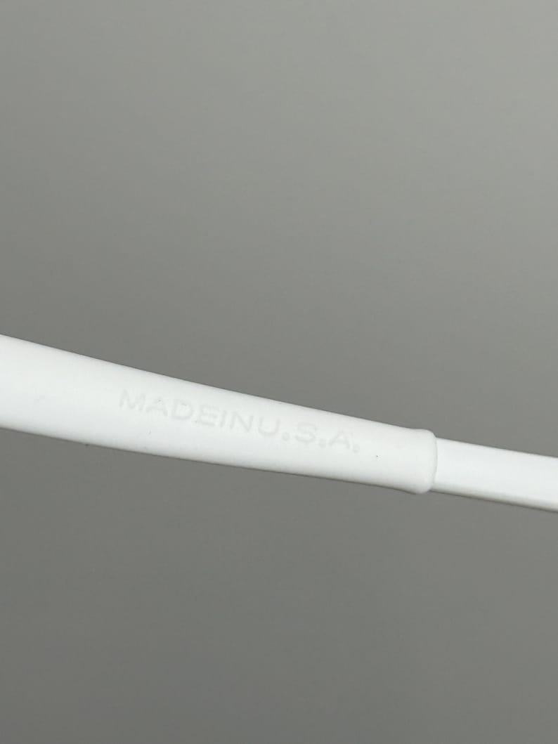 May include: Close-up of a white object with the text "MADE IN U.S.A." printed on it. The object appears to be a part of a larger item, possibly a handle or a component of a tool or device. The background is a solid grey.