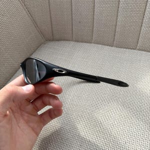 May include: Black sunglasses with a streamlined design. The sunglasses feature dark lenses and a black frame, with a small silver logo on the temple. The arms are slender and extend to the ear pieces.
