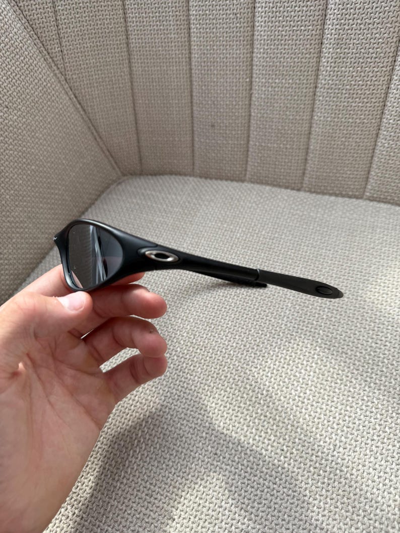 May include: Black sunglasses with a streamlined design. The sunglasses feature dark lenses and a black frame, with a small silver logo on the temple. The arms are slender and extend to the ear pieces.