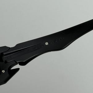 May include: Close-up of black sunglasses with the text "MADE IN U.S.A." printed on the arm. The sunglasses have a sleek, modern design with a matte finish. The frame is a solid black color.