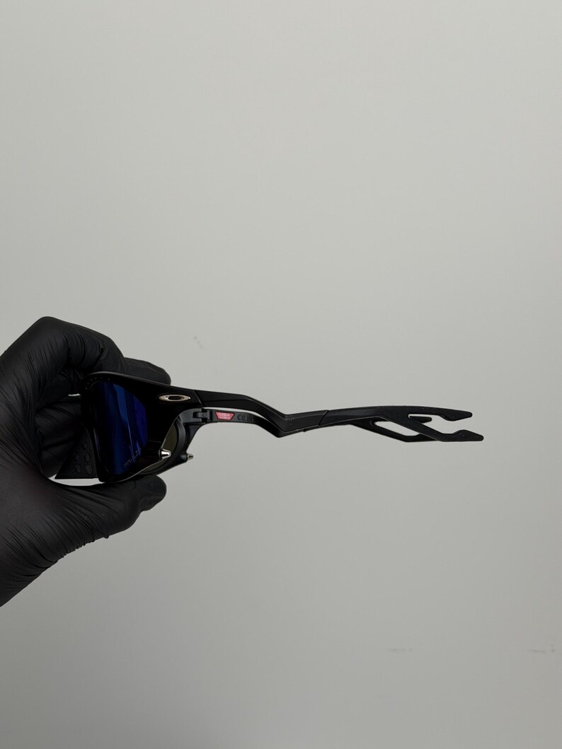 May include: Black sunglasses with blue lenses. The sunglasses have a sleek, modern design with a black frame and arms. The lenses are a vibrant blue color, and the overall look is sporty and stylish.