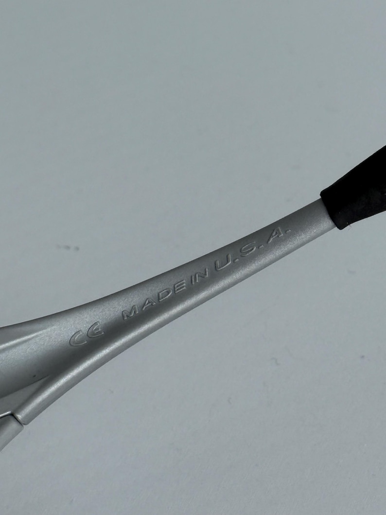 Pu&ograve; includere: Primo piano di un'asta di occhiali argentata con un'estremit&agrave; nera. Il testo "CE MADE IN U.S.A." &egrave; stampato sull'asta. Lo sfondo &egrave; grigio chiaro.