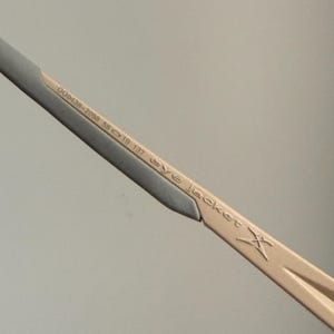 May include: Close-up of a portion of eyeglasses. The frame is a light tan color with a silver accent. The text "OO9438-2058 58 19 137 eye jacket X" is printed on the frame.