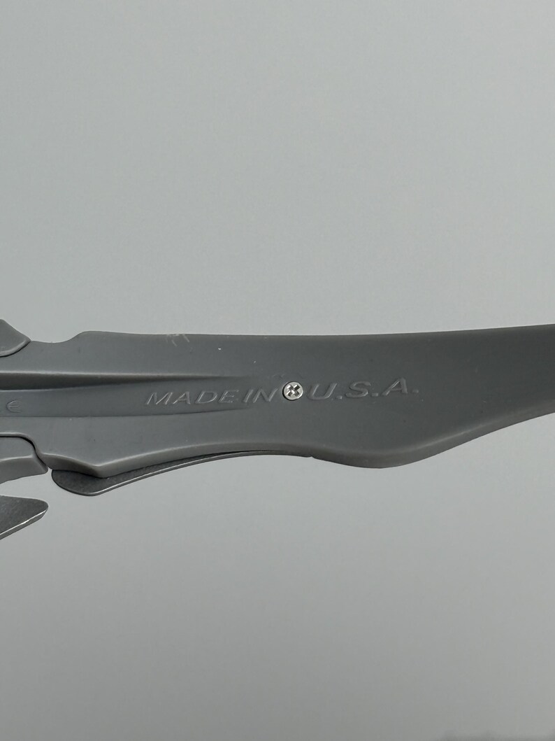 May include: A close-up shot of a gray plastic object with the text "MADE IN U.S.A." printed on it. The object has a curved, aerodynamic shape and appears to be a component of a larger product. The background is a plain, light gray.