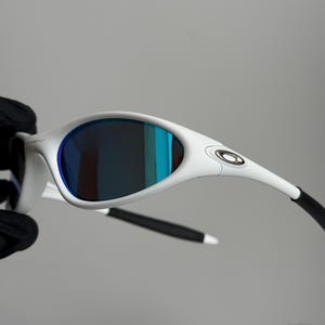 May include: White sunglasses with blue mirrored lenses. The sunglasses have a sleek, modern design with a white frame and black arms. The lenses reflect shades of blue and green.